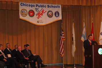 Top Page Eight. Men on stage with Mayor Daley speaking. October 15,  2007. Chicago Mayor Richard M. Daley (above right, at podium) speaks at the commissioning of the Chicago Marine Military Academy high school  in the old Grant Elementary School building at 145 S. Campbell in Chicago. The Marine military academy high school is the fifth military high school in Chicago, and Daley has announced that in the 2008-2009 school year the Chicago Board of Education will open a sixth military academy public high school, that one an “Air Force” high school. The banner above the stage above is for the military and ROTC programs of Chicago’s public schools. On stage, above, are (left to right) U.S. Congressman Rahm Emmauel, who acquired a half million dollars in earmarked funding for the Marine project, Retired Marine General Michael Mulqueen, and Chicago Schools CEO Arne Duncan. Substance photo by George N. Schmidt.